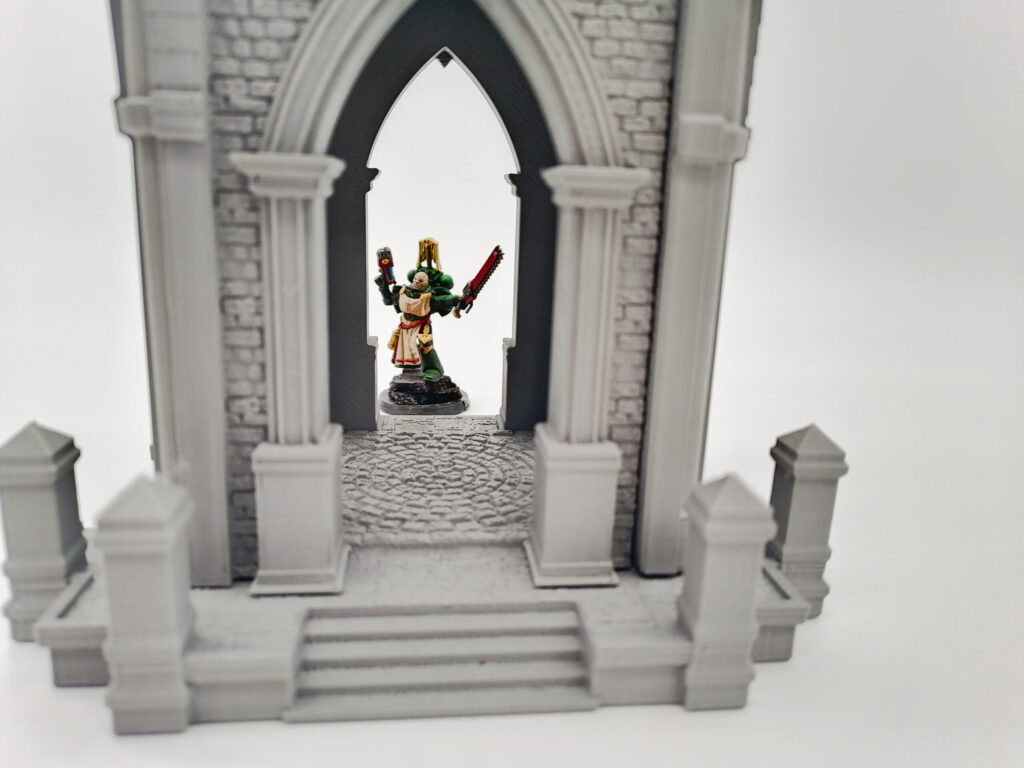 Grey 3D printed Gothic archway tabletop gaming terrain with a painted miniature figure standing in the doorway