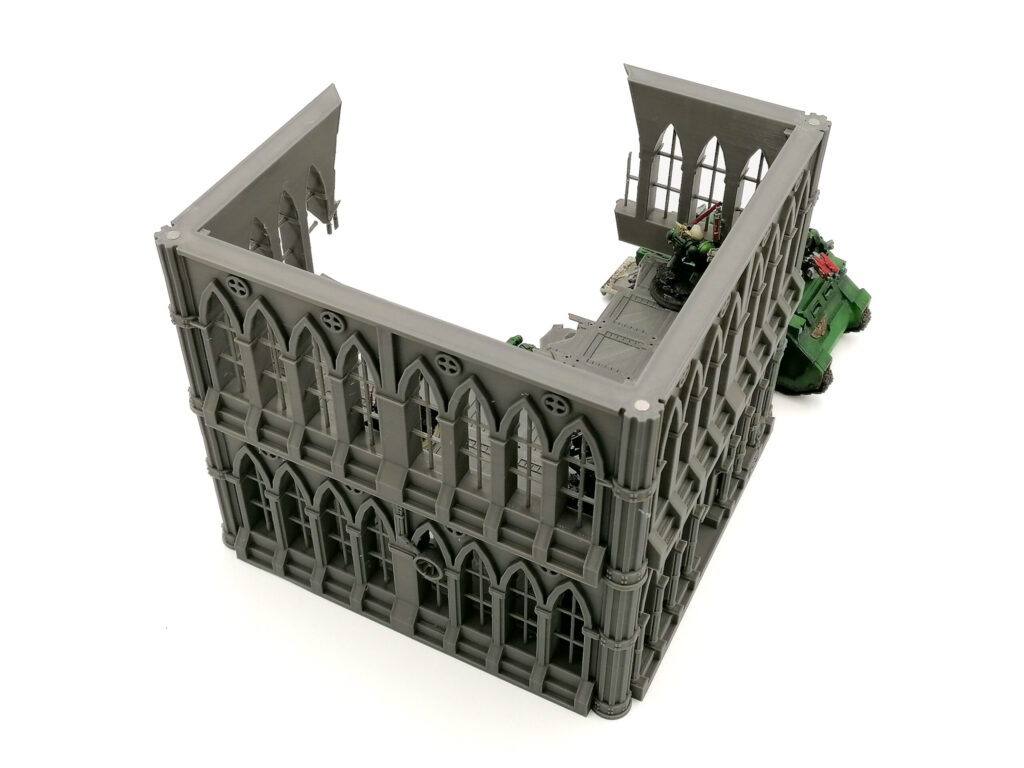 Grey 3D-printed gothic-style ruined building terrain for tabletop wargames, shown with miniature figures