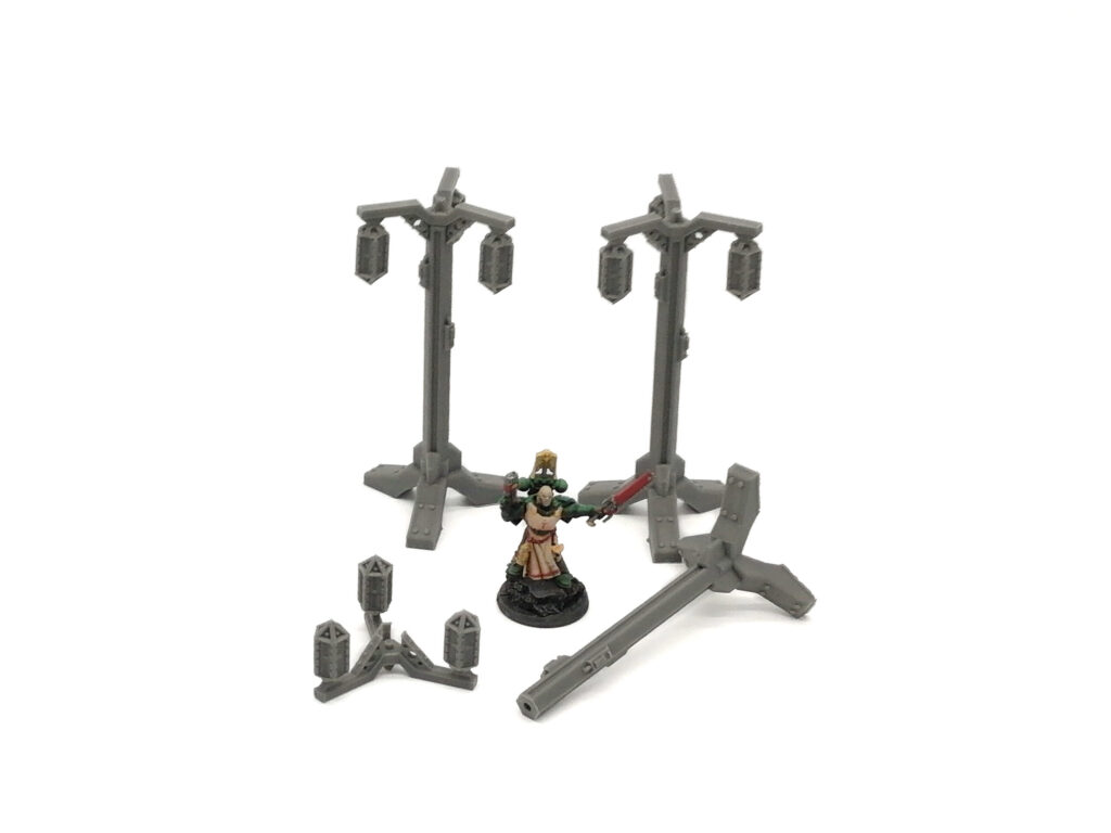 Grey 3D printed miniature street lamps for tabletop gaming, arranged with a painted miniature figure for scale