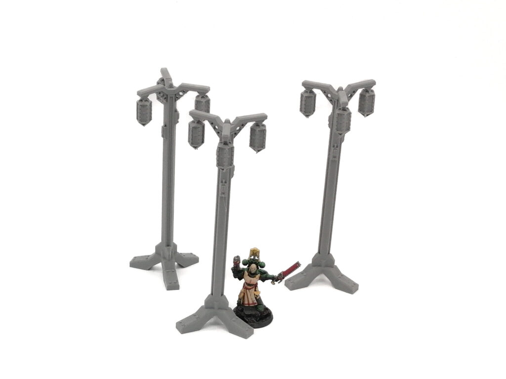 Three grey 3D-printed miniature lampposts on a white background, shown next to a painted figure for scale
