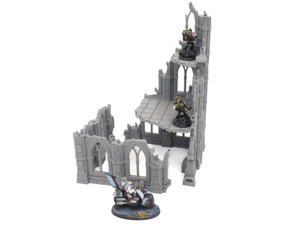 Grey 3D-printed gothic ruin tabletop gaming terrain, shown with miniature figures for scale