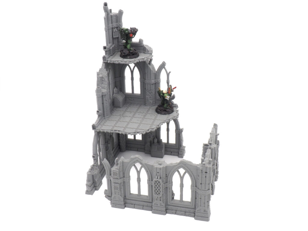 Grey 3D-printed gothic ruin tabletop terrain piece with multiple levels, shown with miniatures for scale