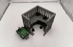 A large stackable ruined gothic themed tabletop wargaming centre piece with a rhino transport next to it