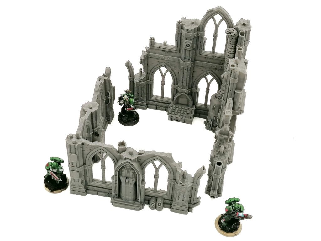 Grey 3D-printed gothic ruin wargaming terrain with arched windows, shown with miniatures for scale