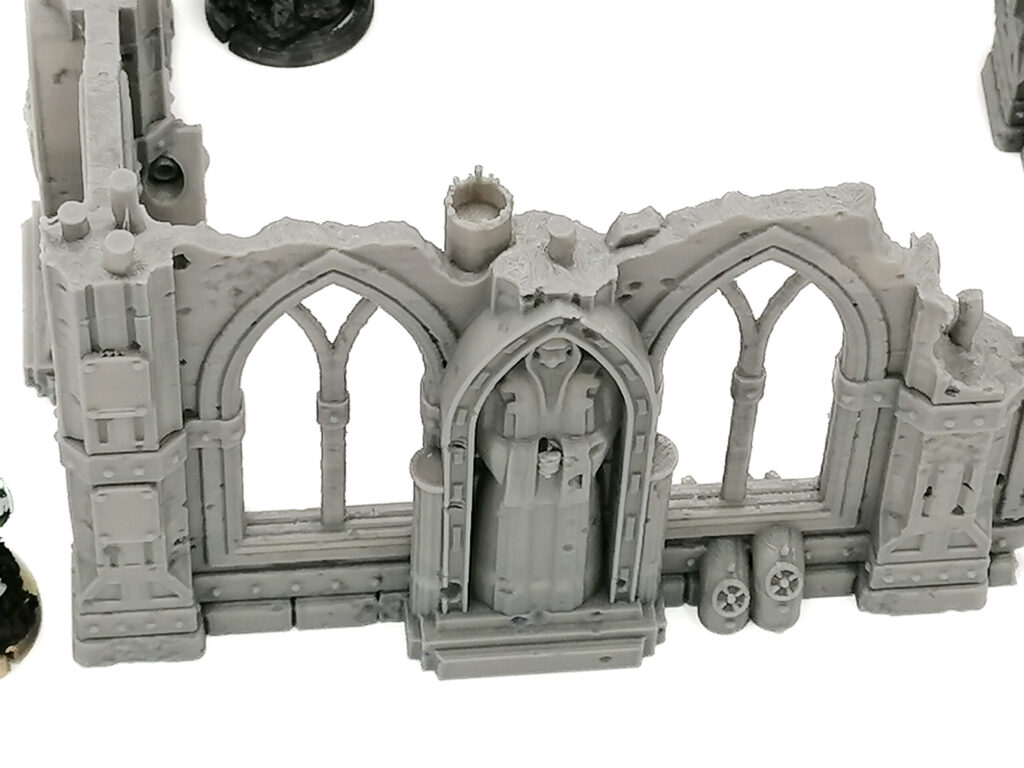 Grey 3D-printed tabletop terrain of a ruined gothic wall with arched windows and a central hooded statue