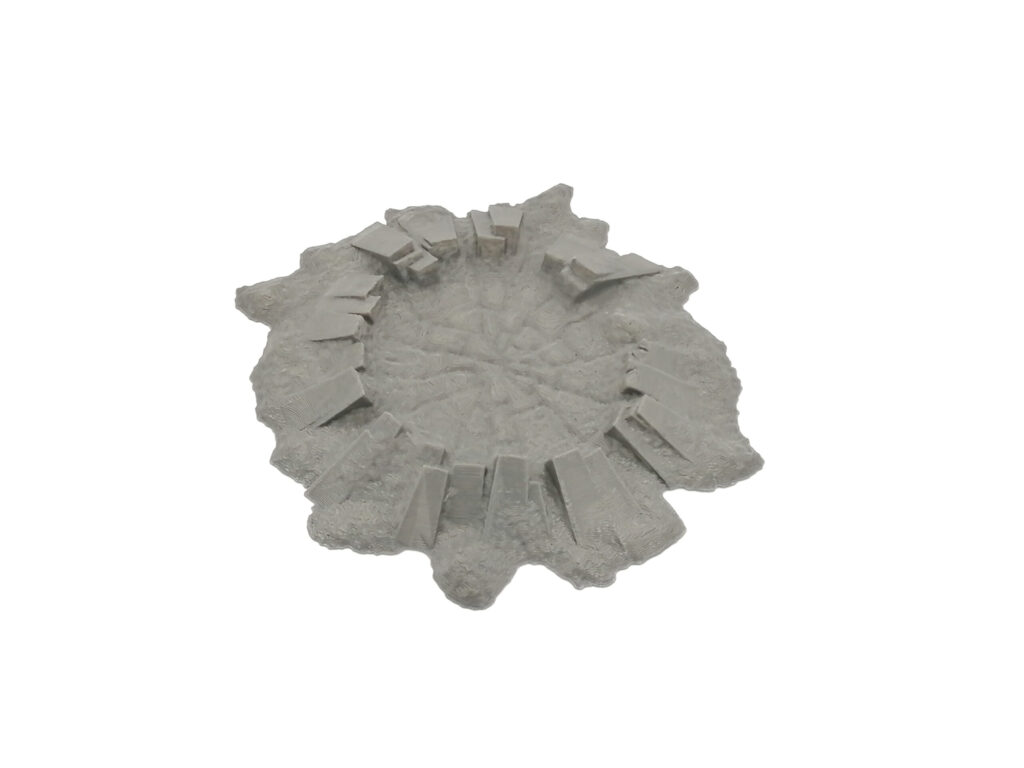 Grey 3D-printed miniature terrain piece of a rocky crater with stone pillars on a white background