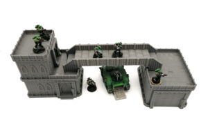 Grey modular sci-fi tabletop terrain with a bridge and buildings, shown with green miniature soldiers and a tank