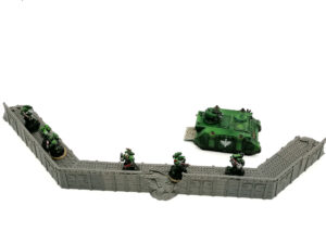 Grey 3D-printed modular defensive wall terrain for tabletop wargaming, shown with miniature figures for scale