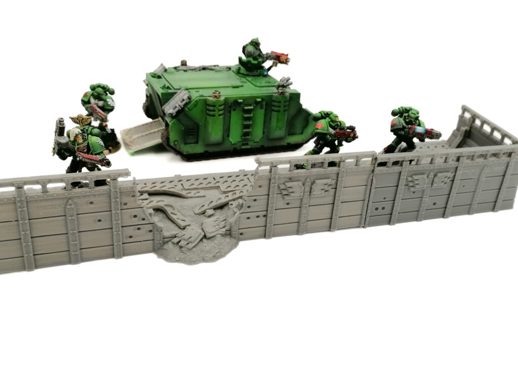 3D-printed grey defensive wall with a breached section, shown with painted sci-fi miniatures for tabletop wargaming