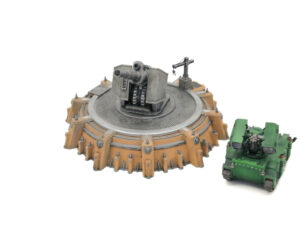 Painted sci-fi gun turret miniature with a circular tan defence fortification, next to a small green tank for scale
