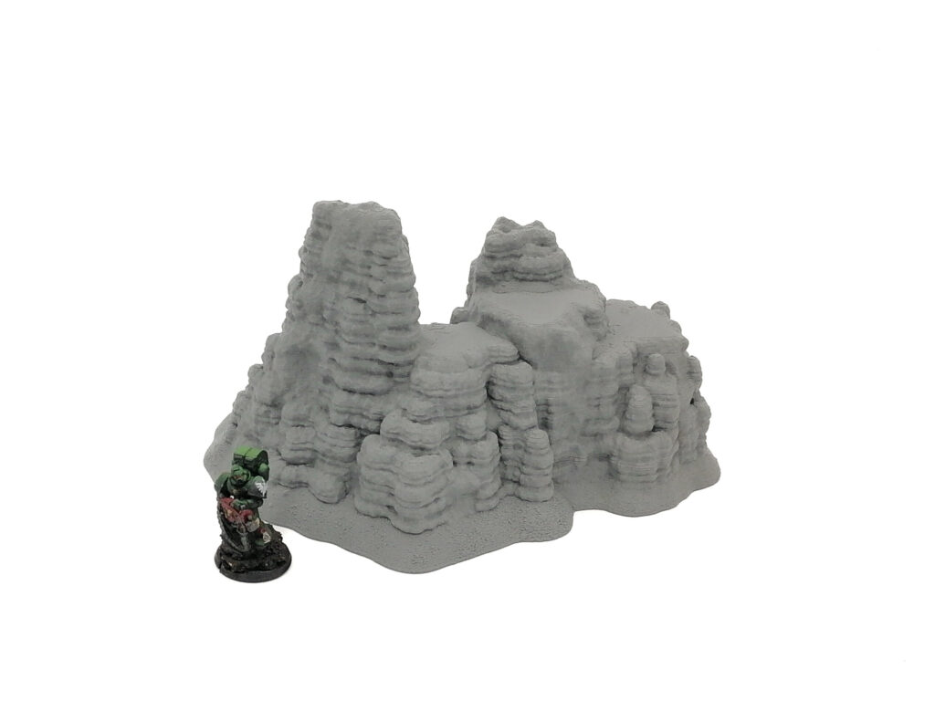 Unpainted grey 3D-printed rocky terrain piece next to a miniature figurine for scale