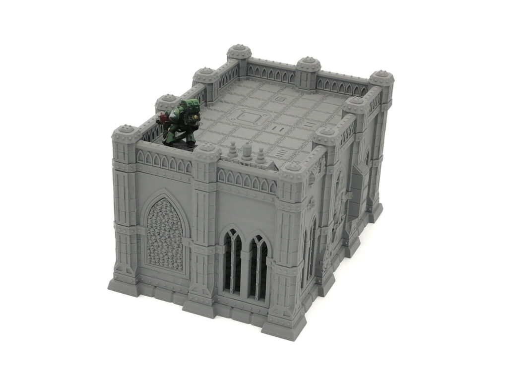 Grey 3D-printed gothic building terrain piece with a small green miniature figure on the roof for scale
