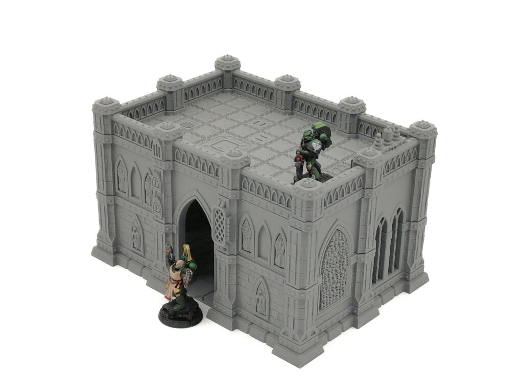 Grey 3D-printed gothic building tabletop terrain with an arched entrance, tiled roof, and miniatures for scale