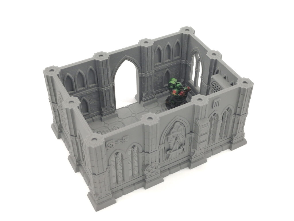 Grey 3D-printed gothic building terrain for tabletop gaming, shown with a miniature figure inside for scale