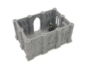 Grey 3D-printed gothic building terrain for tabletop gaming, shown with a miniature figure inside for scale