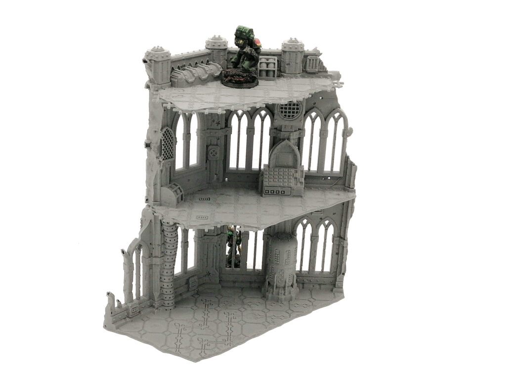 Three-storey grey 3D-printed gothic ruin terrain for tabletop gaming, with a miniature figurine for scale