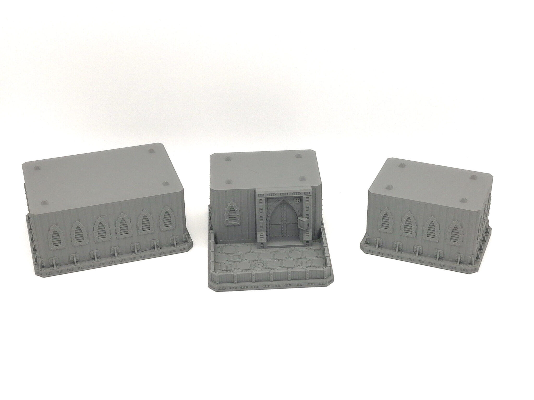 Three grey 3D-printed gothic miniature building sections for tabletop gaming, featuring arched windows and a gated entrance
