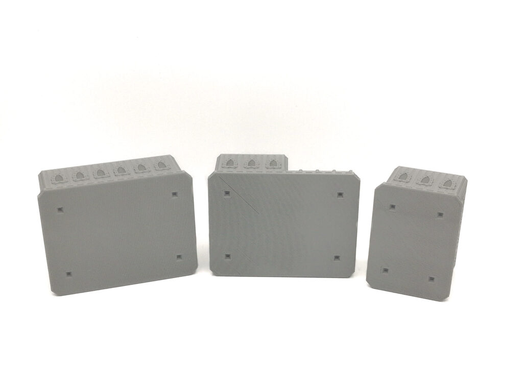 Three grey 3D-printed tabletop terrain pieces showing flat undersides with square connection sockets on a white background