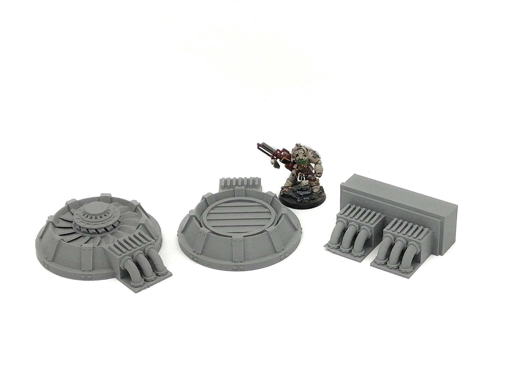 Three unpainted grey 3D-printed sci-fi industrial terrain pieces shown next to a miniature figure for scale