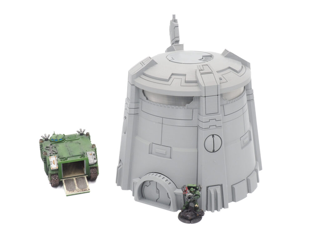 Grey 3D-printed sci-fi tower terrain piece shown with painted wargaming miniatures for scale