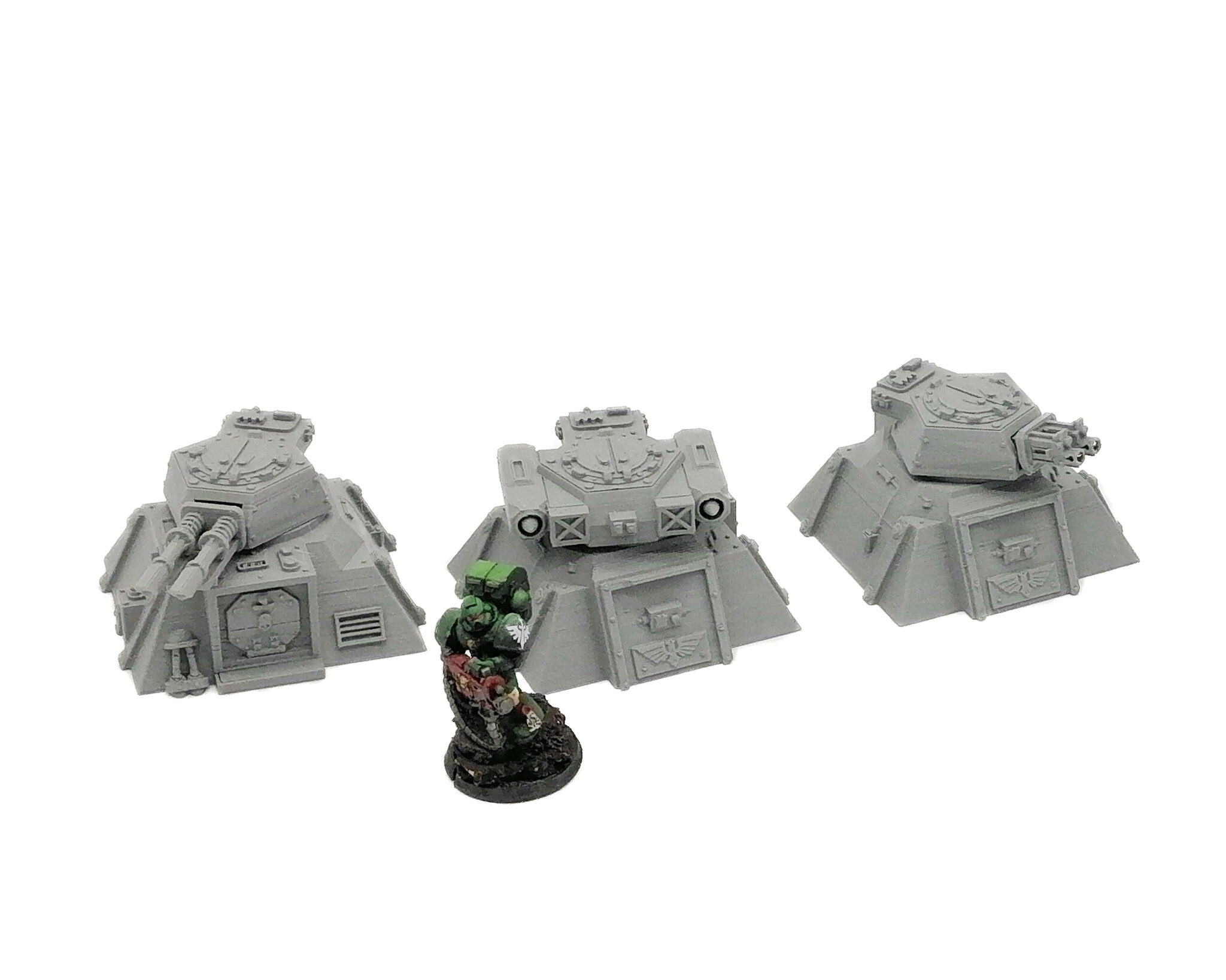 Three grey 3D-printed miniature sci-fi bunkers with weapon turrets, shown next to a painted soldier for scale