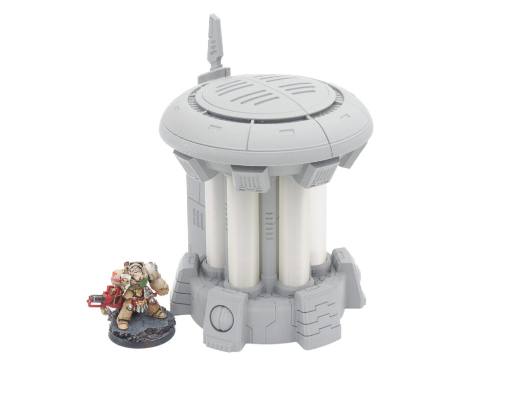 Grey and white 3D-printed sci-fi tower terrain piece shown next to a painted miniature figurine for scale