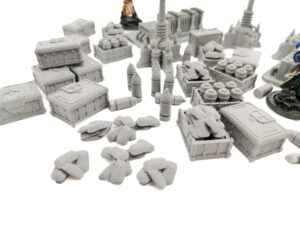 Grey 3D-printed tabletop wargaming terrain miniatures including crates, sandbags, and artillery shells