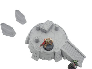 Grey 3D-printed sci-fi tabletop terrain featuring a circular platform, stairs, crates, and miniatures for scale