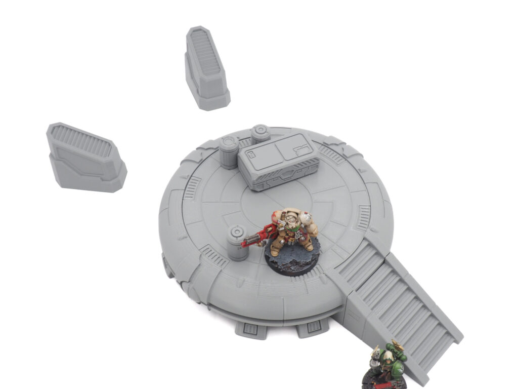 Grey 3D-printed sci-fi platform terrain with stairs and crates, shown with tabletop miniatures for scale