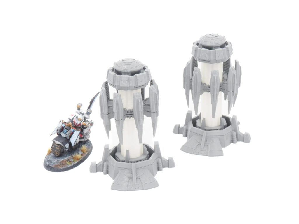 Two 3D-printed sci-fi tower terrain pieces shown next to a painted miniature biker for scale