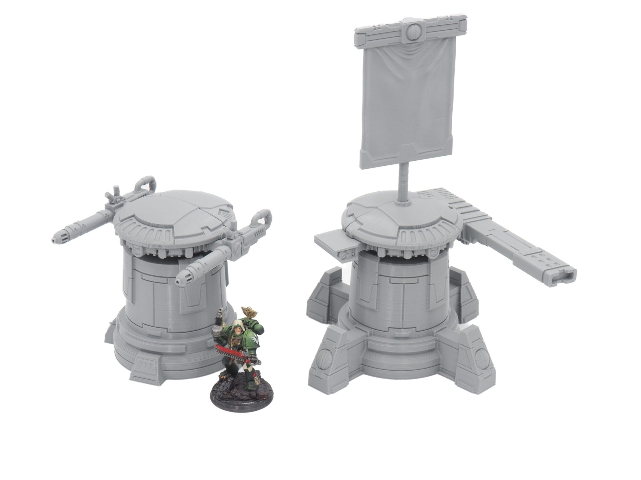 Two grey 3D-printed sci-fi turrets, one with cannons and one with a banner, next to a painted miniature for scale