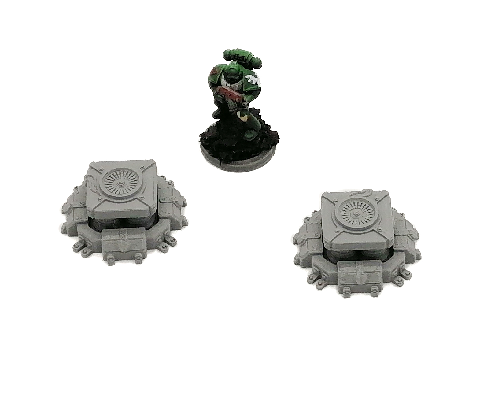 Two unpainted grey 3D-printed sci-fi tabletop terrain pieces next to a painted miniature soldier for scale