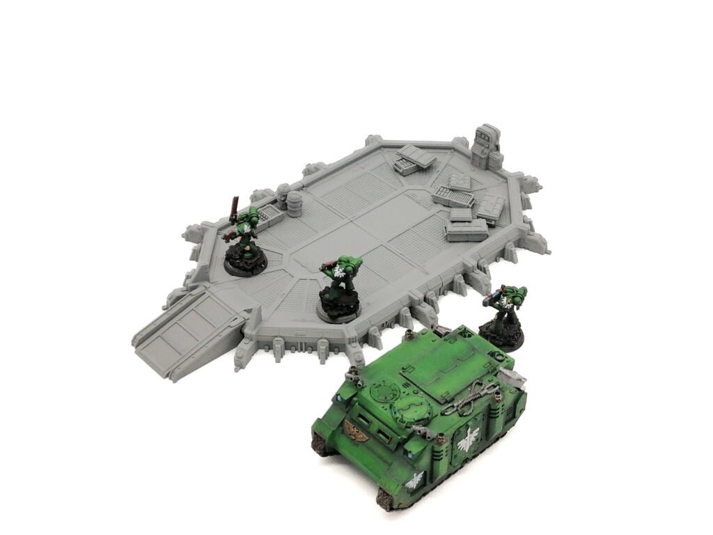 Grey 3D-printed sci-fi landing pad terrain for tabletop gaming, shown with painted miniatures to illustrate scale