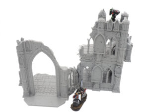 Grey 3D printed gothic ruins tabletop gaming terrain, featuring a ruined tower and archway with miniatures for scale