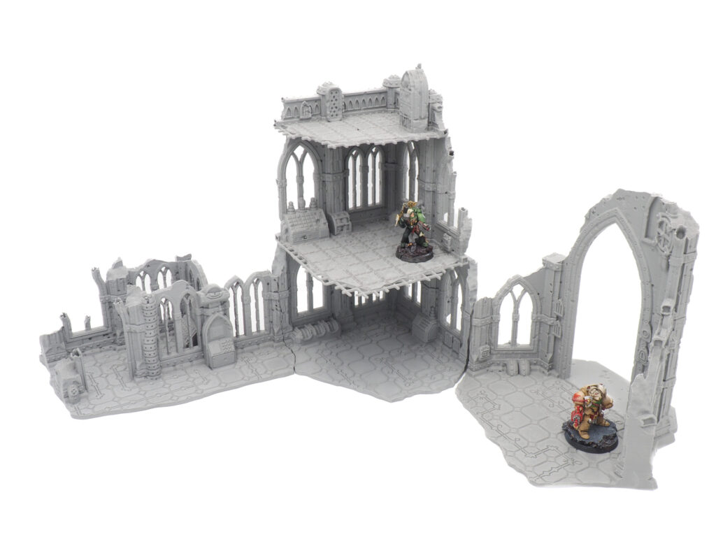 Grey 3D printed gothic ruins tabletop terrain set, shown with two painted miniature figures for scale