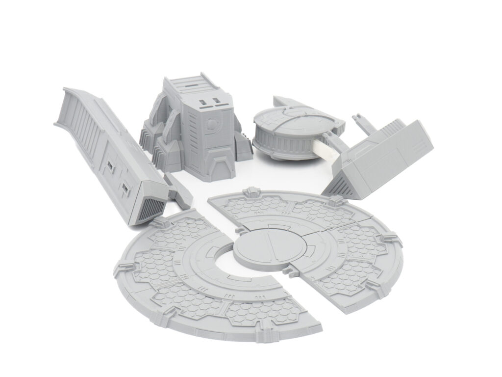 Grey 3D-printed sci-fi tabletop terrain kit, featuring modular building components and a circular landing pad