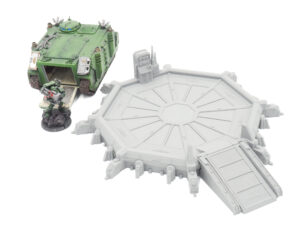Grey 3D-printed sci-fi landing pad terrain with ramp, pictured alongside painted miniatures for scale