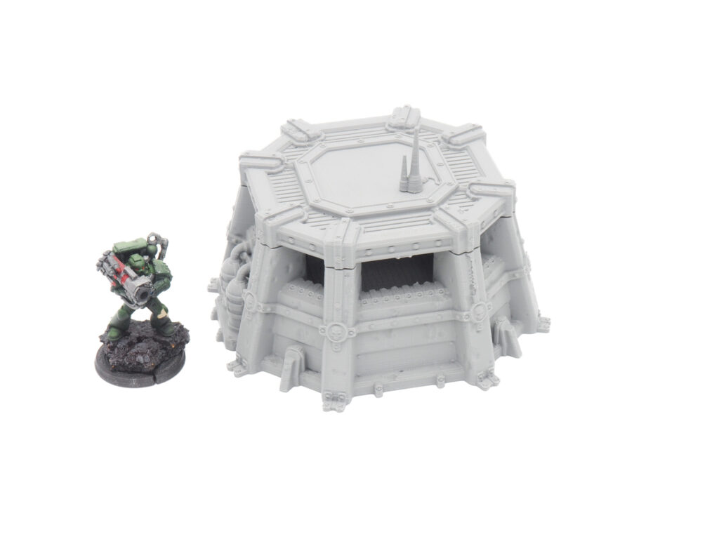Grey 3D-printed sci-fi bunker terrain model next to a painted miniature soldier for scale
