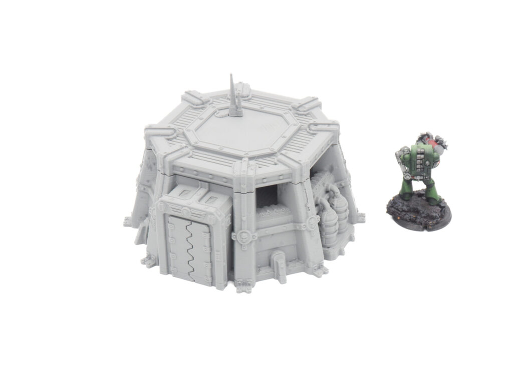 Grey 3D-printed sci-fi bunker terrain model next to a painted miniature figure for scale
