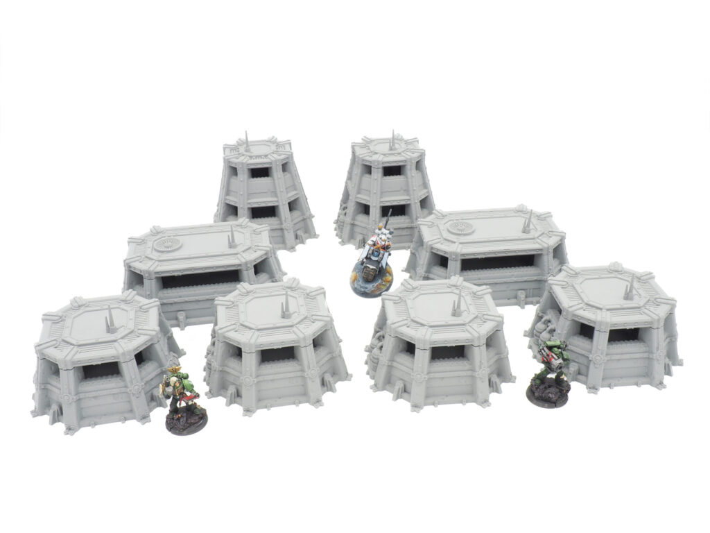 Modular grey 3D-printed sci-fi miniature bunkers and pillboxes for tabletop gaming, shown with figures for scale