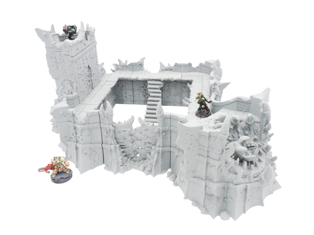 Modular grey 3D-printed fortress terrain for tabletop gaming, shown with painted miniature figures for scale