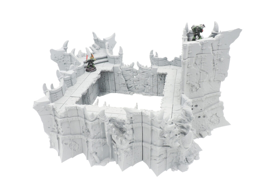 Grey 3D-printed ruined fortress walls for tabletop wargaming, shown with miniature figures for scale