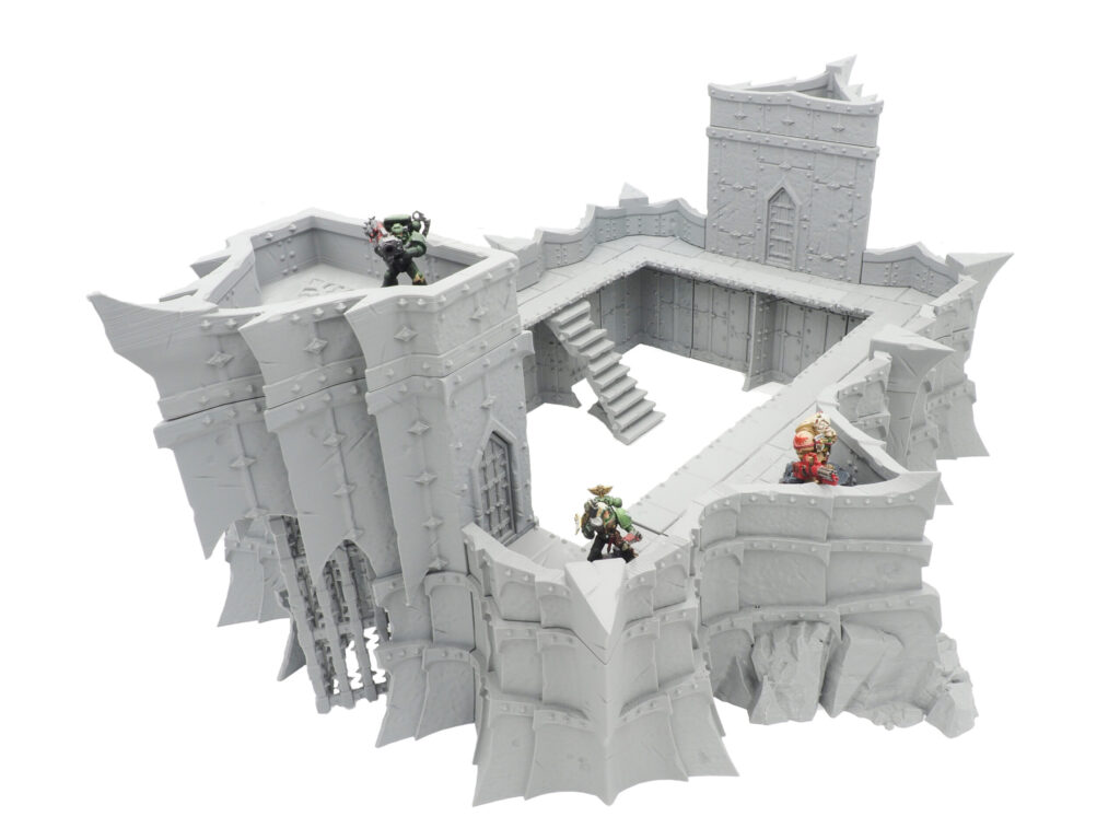 Grey 3D-printed tabletop wargaming fortress terrain with ramparts, stairs, and painted miniatures