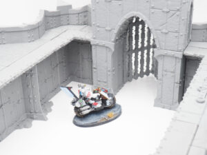 Grey 3D-printed modular fortress walls and gatehouse, shown with a painted miniature motorcycle rider for scale