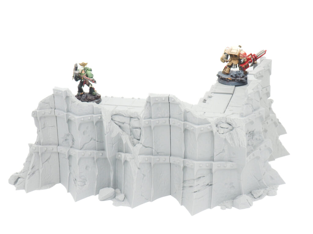 Grey 3D-printed sci-fi fortification wall terrain with two painted gaming miniatures standing on top