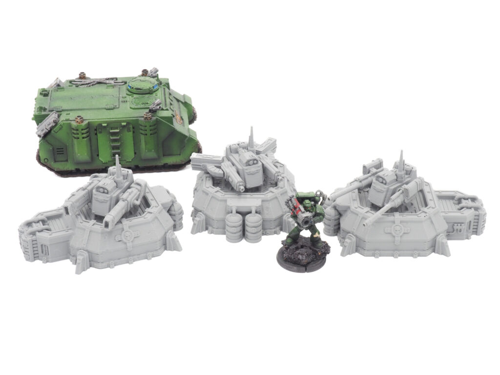 Three grey 3D-printed miniature turrets displayed next to a painted green sci-fi tank and soldier for scale
