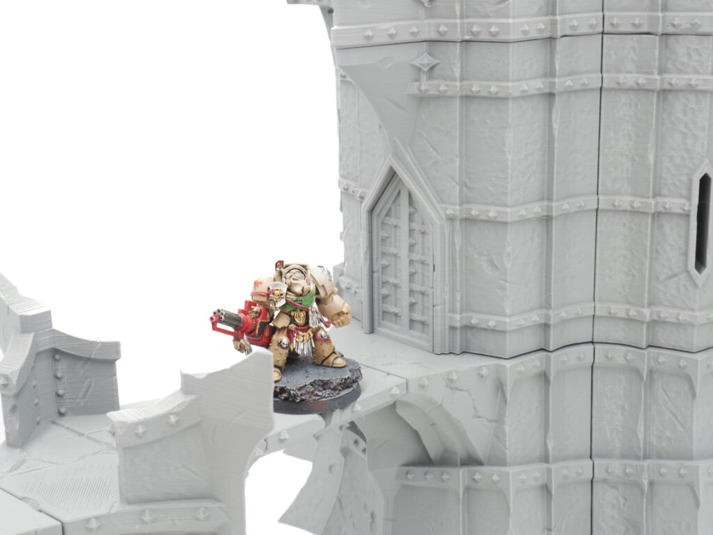 Grey 3D printed castle tower and bridge tabletop terrain with a painted miniature standing on the walkway