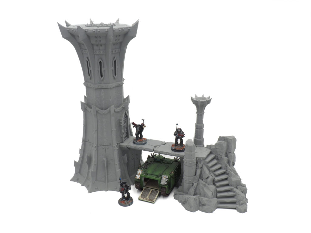 Grey 3D-printed gothic tower and ruins terrain, shown with miniature gaming figures and a vehicle for scale