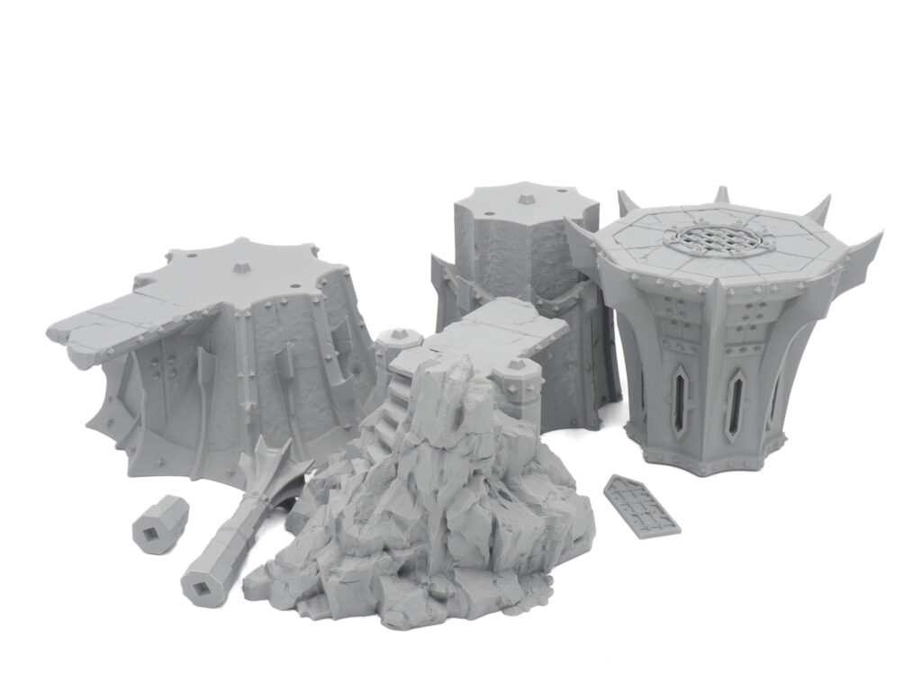 Grey 3D printed tabletop miniature terrain pieces, including Gothic pillars and a rocky outcrop, on a white background