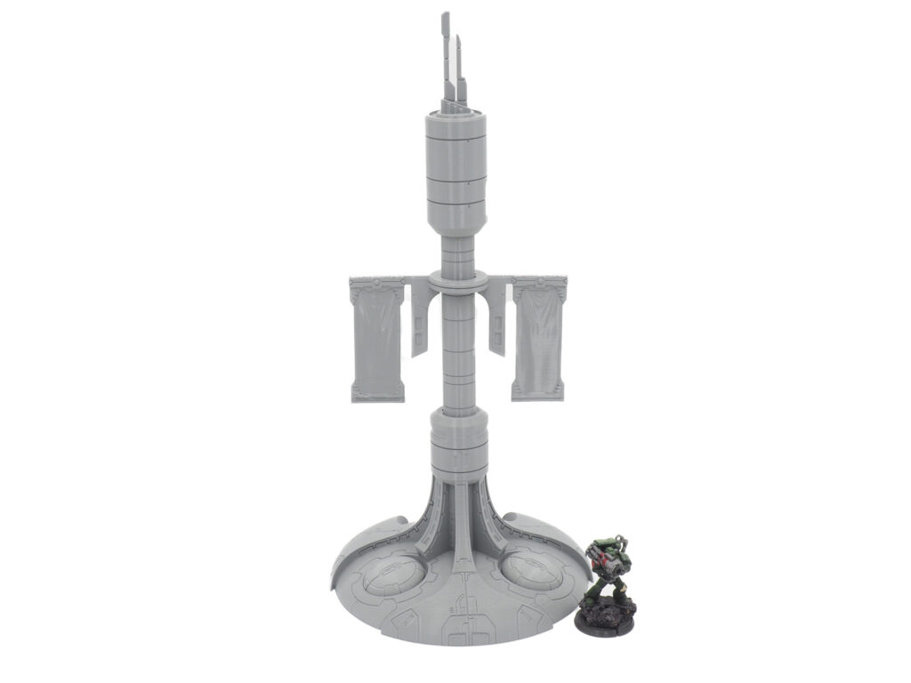 Grey 3D-printed sci-fi tower terrain with banners, pictured next to a small tabletop miniature for scale
